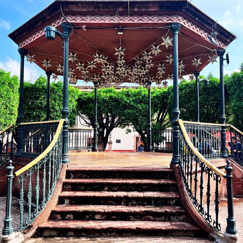 Entrance to El Jardín Kiosk in San Miguel de Allende, featuring terracotta tones, worn-out stairs, and decorative aluminum stars hanging from the roof.