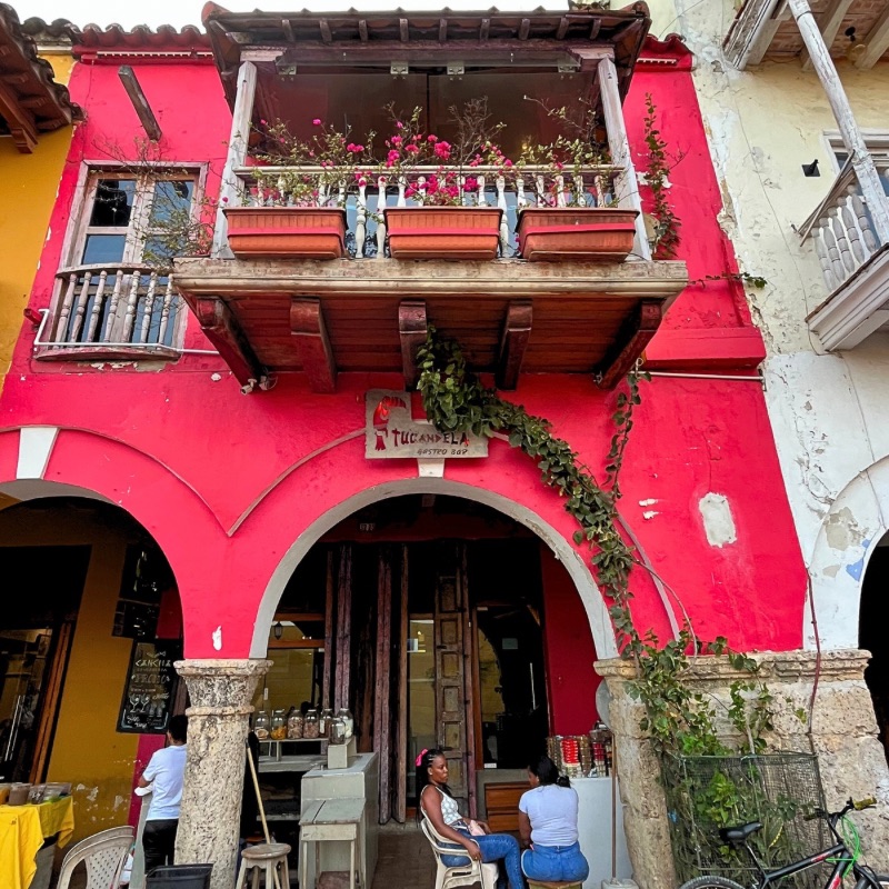 A coral red-walled colonial home and shop in Cartagena with a wooden balcony and blooming bougainvillea.