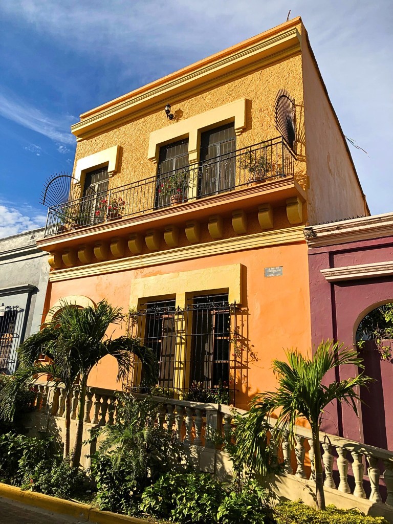 The architecture along Ángel Flores Street showcases Mazatlán’s colonial charm, with bold colors, wrought-iron balconies, and tropical plants adding life to the scene.