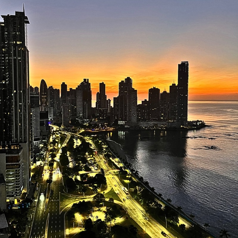 Red sunset casting a fiery glow behind the high-rise buildings along the Cinta Costera in Panama City, with silhouettes of towers outlined against a deep, glowing sky.