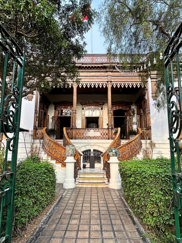 The grand facade of the historic Berninzon mansion in Barranco, Lima, showcasing its ornate wooden balconies, sweeping staircase, and lush greenery.