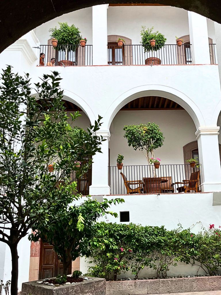 Interior terrace of Casa de Mayorazgo de la Canal with white colonial walls, elegant arches, green potted plants, and thick wooden doors that open into shaded stillness.