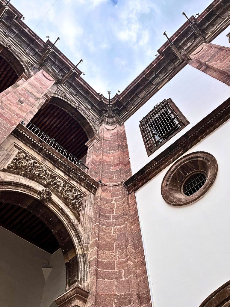 Corner of Casa de Mayorazgo de la Canal’s interior courtyard showing pink stone and white walls meeting under a clear blue sky, embodying colonial elegance and architectural balance.