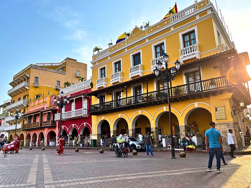 Late afternoon street scene in Cartagena’s Walled City, with people walking and chatting under golden-hour light.