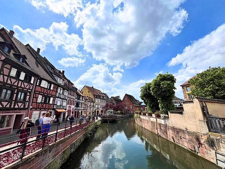 Colmar canal scene with historic Alsace half-timbered houses under a partly cloudy sky.