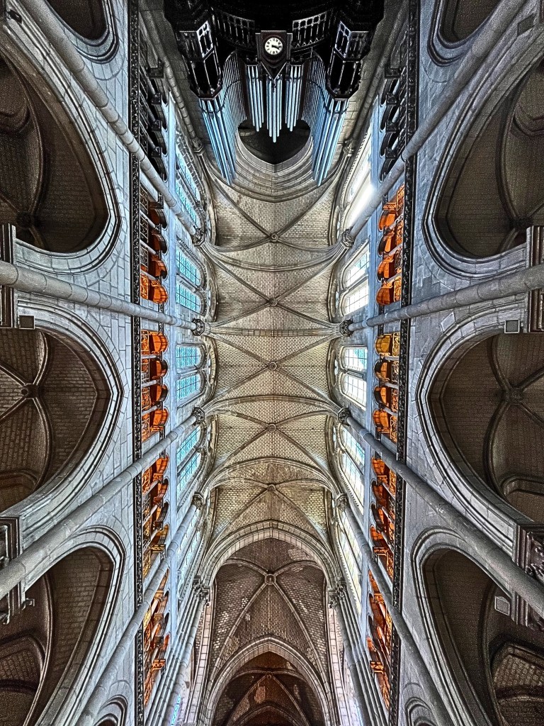 Vertical view of the ribbed vaulted ceiling at Basilique Saint-Nicolas in Nantes, France, featuring Gothic arches, stained glass lancet windows, and a grand organ.