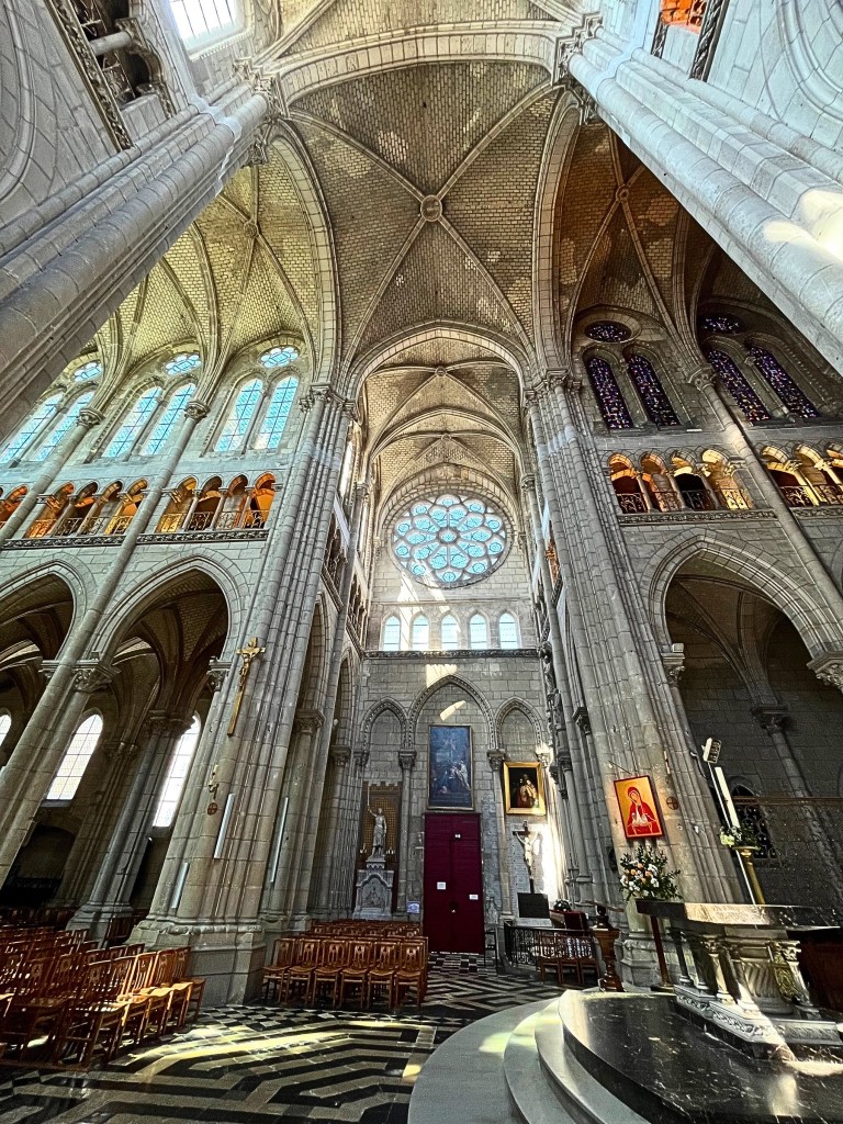 Nave and transept crossing of Basilique Saint-Nicolas in Nantes, featuring Gothic ribbed vaults, rose window, stained glass, clustered columns, and altar platform.