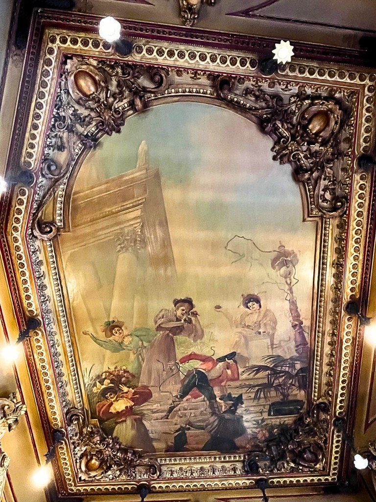 Ceiling frescoes with swirling designs and muted colors, adding to the poetic ambiance of the historic brasserie.