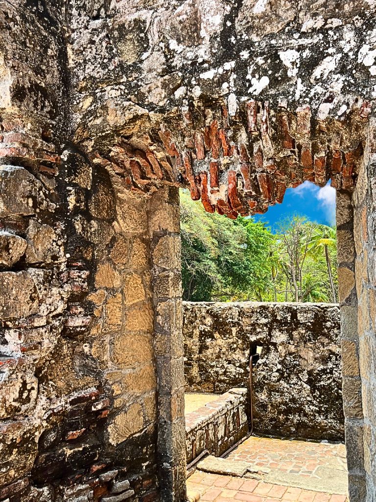 Close-up of a stone doorway in the ruins of Old Panama City, opening to a corridor and terrace with a view of a tree and the blue sky beyond.