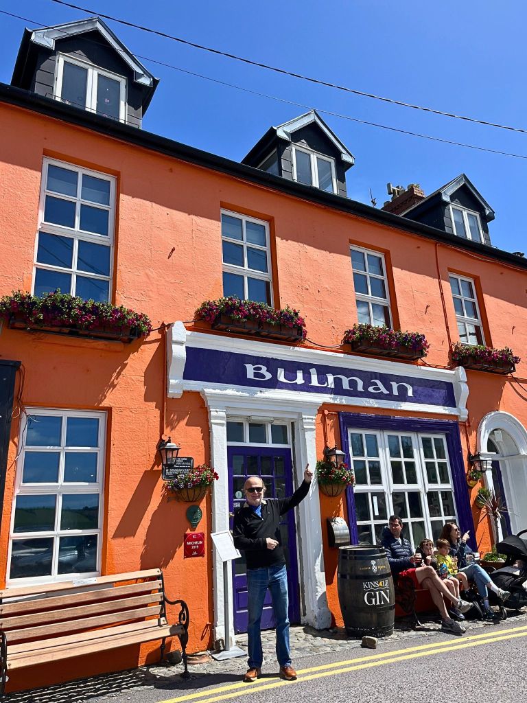 Man smiling in front of The Bulman pub in Kinsale, Ireland, with the pub’s sign and stone exterior in the background.