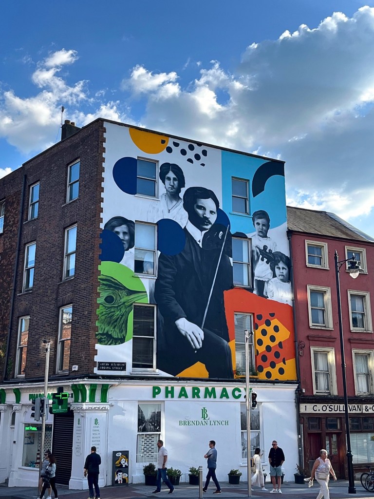 The mural honors Tomás MacCurtain, Cork’s Lord Mayor in 1920 and a prominent leader during Ireland’s fight for independence, as well as a noted musician who championed Cork’s cultural heritage. He’s portrayed with his fiddle, surrounded by his wife and children—symbolizing both his public impact and personal ties.
