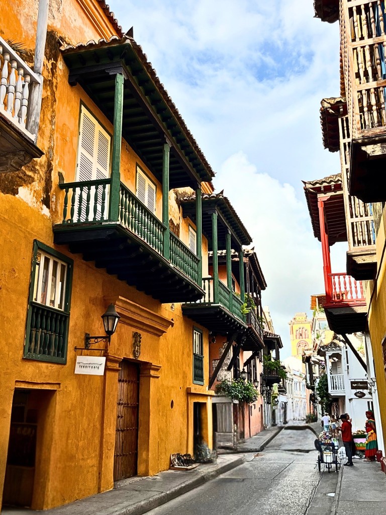 Lively street scene in Cartagena’s Walled City, featuring colorful colonial buildings with wooden balconies and a street vendor on the right.