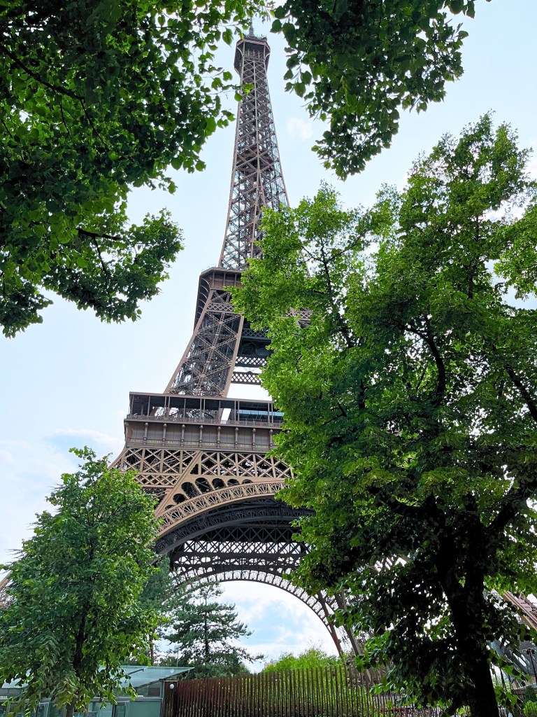 Paris Eiffel Tower framed by leafy trees and glowing clouds.